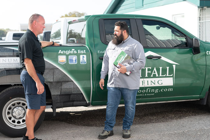 two men standing at the side of a Westfall Roofing pickup truck