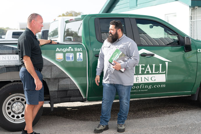 two men standing at the side of a Westfall Roofing pickup truck in Tampa