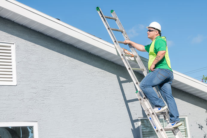 Roofer in safety gear on a ladder at the edge of a roof