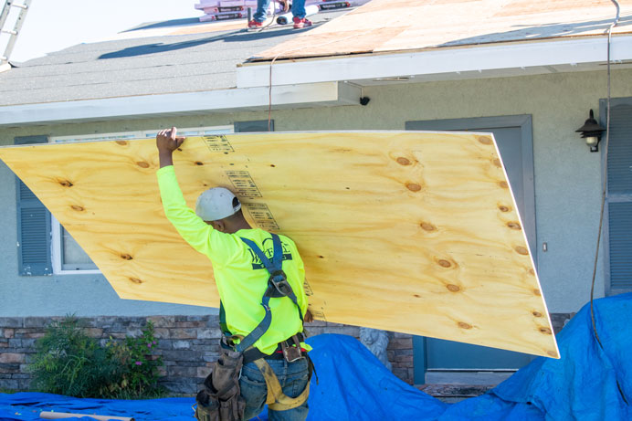 roofer carrying plywood to repair a storm damaged roof