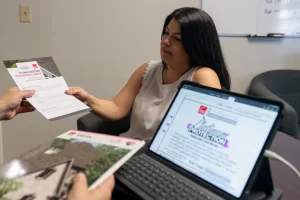 Anissa Westfall handing a client a warranty packet. Computer screen with Owens Corning Platinum Protection warranty on the screen.
