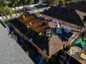 Westfall workers on a roof installing shingles. Packs of shingles are on the roof. Workers have fall protection in place.